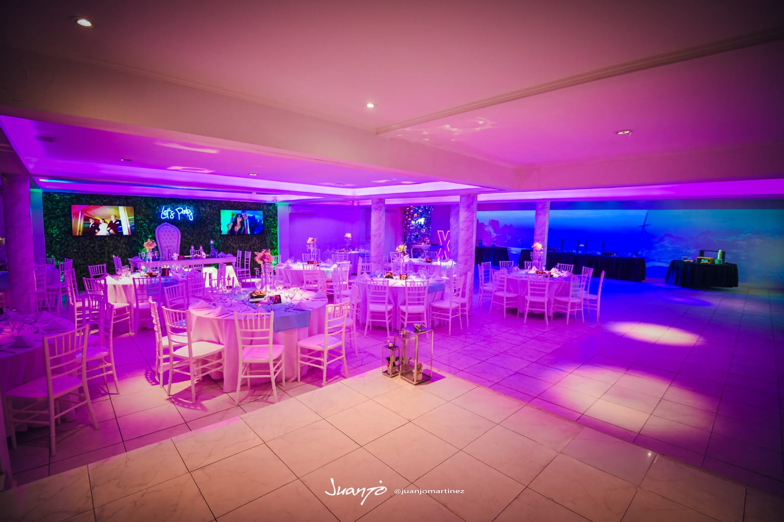 Salón principal con mesas vestidas en blanco e iluminación violeta